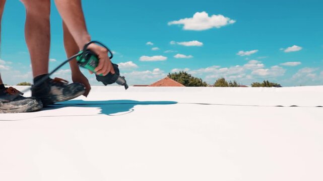 Construction worker installing pvc roofing membrane with hot air gun
