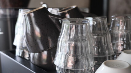 Transparent glass cups stacked upside down next to ceramic mugs, neatly arranged in a cafe environment for serving coffee or tea.  
