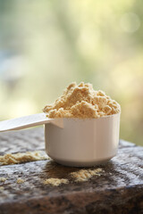 Whey protein powder in a plastic measuring spoon outdoors