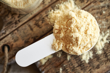 Whey protein powder in a measuring spoon on a table, top view