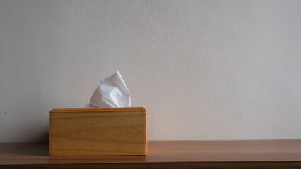 A minimalist wooden tissue holder with a single white tissue sheet pulled out, placed on a wooden...