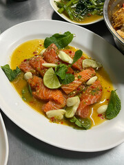 Thai style raw salmon spicy salad with lime, garlic, chili, and fresh mint leaves served in citrus sauce on white plate, authentic Southeast Asian seafood appetizer