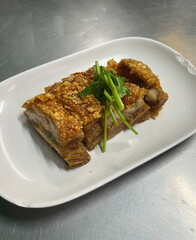 Crispy roasted pork belly with crunchy golden skin and tender juicy meat slices garnished with fresh cilantro served on white plate, traditional Asian cuisine dish
