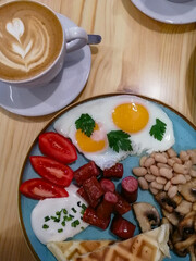 breakfast of fried eggs, sausages, beans, mushrooms and tomatoes accompanied by aromatic signature coffee