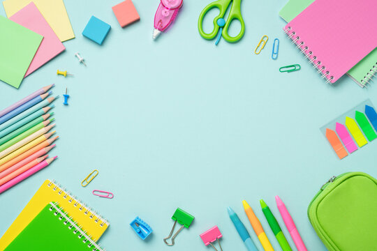 Supplies flat lay on blue background. Notepads, markers, pensils, paper clips and cissors. Flat lay image. Frame with space for design.