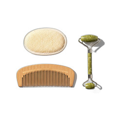 A still life of a wooden comb, loofah sponge, and green jade facial roller on a black backdrop