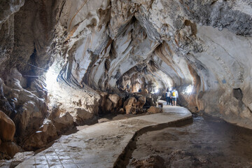 Jang Cave, Vang Vieng, Laos, Tourists walking inside limestone cave with paved pathway and natural light  in Luang Prabang, Laos