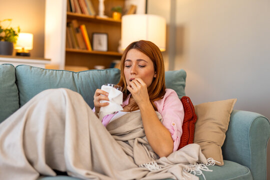 A sick woman is taking medicine, holding a pill and a glass of water. The image captures a moment of self-care and recovery, reflecting themes of illness, treatment, and healthcare.