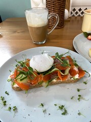 Smoked salmon and poached egg on toast with vegetables and latte on wooden table in cafe setting