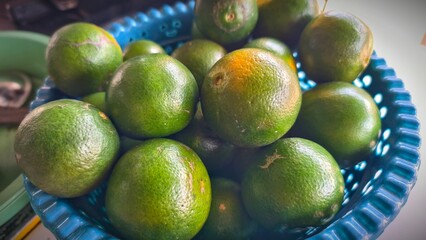 A delightful collection of green oranges in a vibrant blue bowl, a testament to nature's bounty,  Green oranges clustered in a blue container