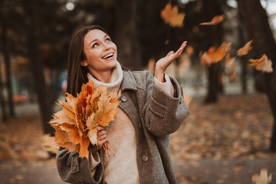 Young woman enjoying autumn park with colorful leaves in hand, portraying a cheerful and stylish seasonal outdoor moment