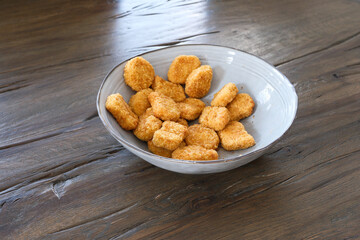 A bowl of fried chicken nuggets sits on a wooden table