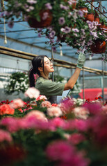 Fototapeta premium Asian woman working in greenhouse holding clipboard inspecting flowers.