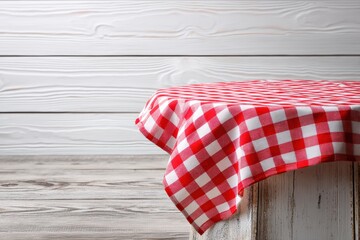 Obraz premium A rustic table covered with a red and white checkered tablecloth stands against a white wooden wall background