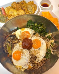 Bibimbap, a vibrant Korean rice dish topped with a variety of seasoned vegetables, gochujang, and a fried egg, often accompanied by sliced meat. Mixed together, it creates a flavorful and balanced.