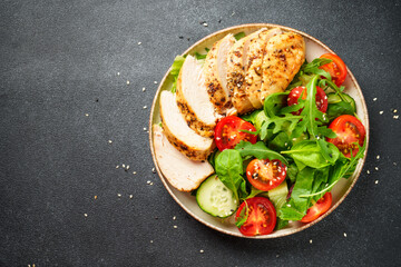 Green salad with grilled chicken meat at black table.
