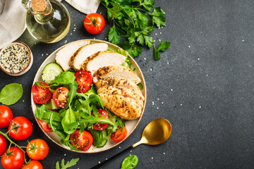 Green salad with grilled chicken meat at black table.