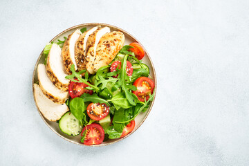 Green salad with grilled chicken meat at black table.