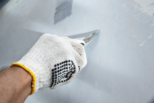 Construction worker in gloves using a scraper to scrape and remove all loose paint on the wall during home renovation. Home renovation project