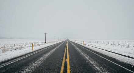 A snow-covered road stretches toward the horizon, vanishing into a hazy white sky, lined with snowy fields and sparse utility poles.