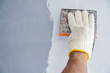 Construction worker in gloves using a scraper to fill cracks and surface imperfections on the wall...