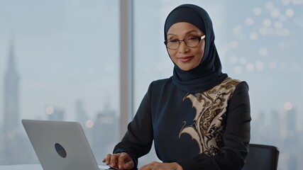 A confident Muslim businesswoman in a hijab working on a laptop in a modern office - Powered by Adobe