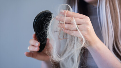 Naklejka premium Young woman with brittle hair holding hairbrush with damaged strands showing early signs of alopecia and hair breakage
