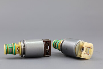 Two Allison transmission solenoid valves are shown on a gray background, one standing upright and the other on its side. The photo highlights their metallic bodies, wires, and connectors. © Jumain