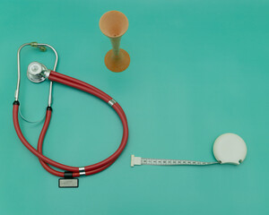 red stethoscope and measuring tape and obstetric wooden stethoscope on green Background, Space for...