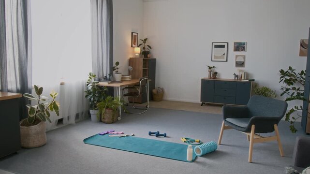 Wide no people shot of living room in home, with sports equipment prepared for home workout, with fitness mat on floor, dumbbells, skpping rope, resistance bands, back roll, water bottle