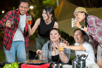Indonesian southeast asian people relaxing together outdoors and enjoying refreshing drinks while cooking sliced beef on a grill pan. The scene of the lifestyle of enjoying food in a natural setting