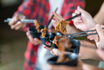 People enjoying a meal, using chopsticks to serve themselves a barbecue meal from small black bowls. The scene of the lifestyle of enjoying food in a natural setting
