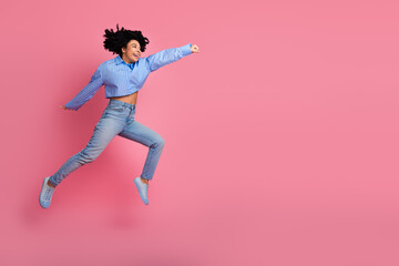 Joyful young woman jumping dynamically against a pink background, expressing energy, happiness, and a carefree lifestyle