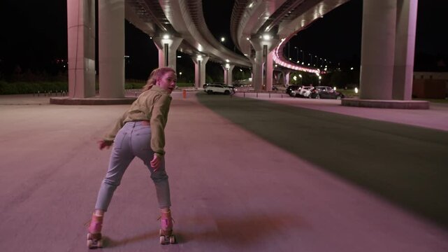 Young woman roller skater dances gliding under bridge at night