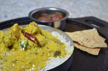 A delicious plate of kadhi chawal served with steamed rice, crispy papad, and a sweet portion of gulab jamun. Authentic Indian comfort food presentation.