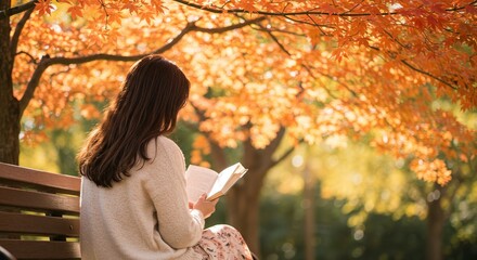 Back view of a woman reading a book on a bench under a maple tree