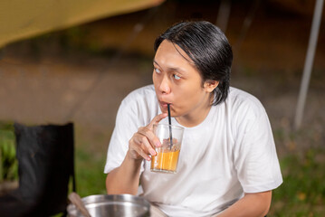 Indonesian southeast asian man relaxing together outdoors and enjoying refreshing drinks while cooking sliced beef on a grill pan. The scene of the lifestyle of enjoying food in a natural setting