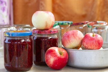 red and yellow apples on the table next to jars of raspberry jam and empty glass jars in the background