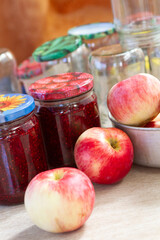 red and yellow apples on the table next to jars of raspberry jam and empty glass jars in the background