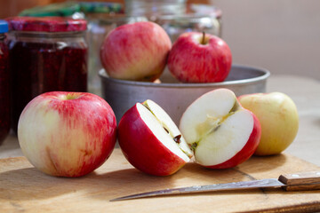 red and yellow apples on the table next to jars of raspberry jam and empty glass jars in the background