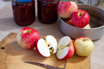 red and yellow apples on the table next to jars of raspberry jam and empty glass jars in the background