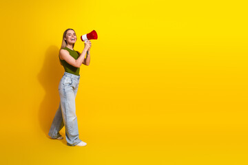 Excited young woman with megaphone in casual outfit posing against vivid yellow background, radiating joyful energy