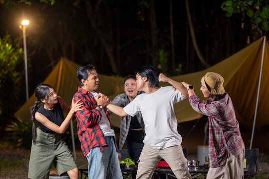 Heated argument escalates between two Indonesian southeast asian men during a camping trip, as concerned friends try to deescalate the situation. Scene of the lifestyle of camping in a natural setting