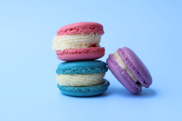 Stack of colorful macarons with generous cream fillings sits isolated against a blue background. These traditional dessert cookies are both delightful and eye catching.