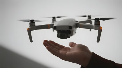 A small drone hovers above an outstretched hand against a plain background.