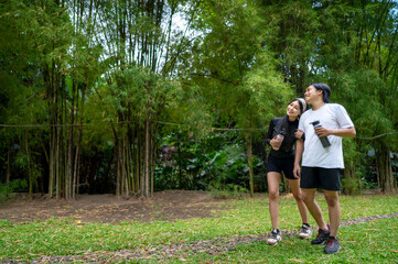 Fototapeta premium Indonesian southeast asian couple in a sporty outfit resting together after a practice exercise in a public park outdoors. Concept of a Healthy active lifestyle