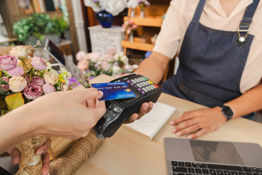 Small business flower owner shop handles payment credit card purchase transaction, Asian florist hand holding bouquet while paying, modern retail store using cashless system for customer convenience