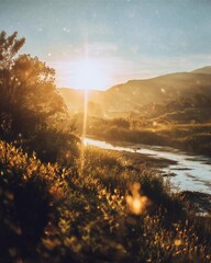 A tranquil landscape featuring a sunset over rolling hills, with golden sunlight illuminating the river and surrounding nature, creating a serene and peaceful atmosphere.