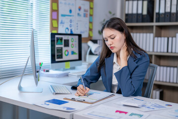 A woman is sitting at a desk with a computer monitor and a clipboard