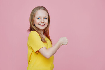 Cheerful young girl in a bright yellow shirt smiling against a pink background, conveying happiness and joy, ideal for children s lifestyle concepts